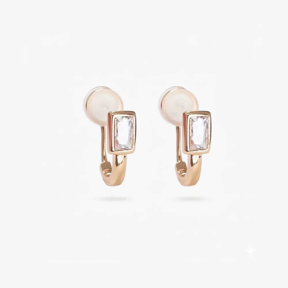 Detailed close-up of gold clip-on earrings with emerald-cut center stone and baguette cubic zirconia accents on a white background.