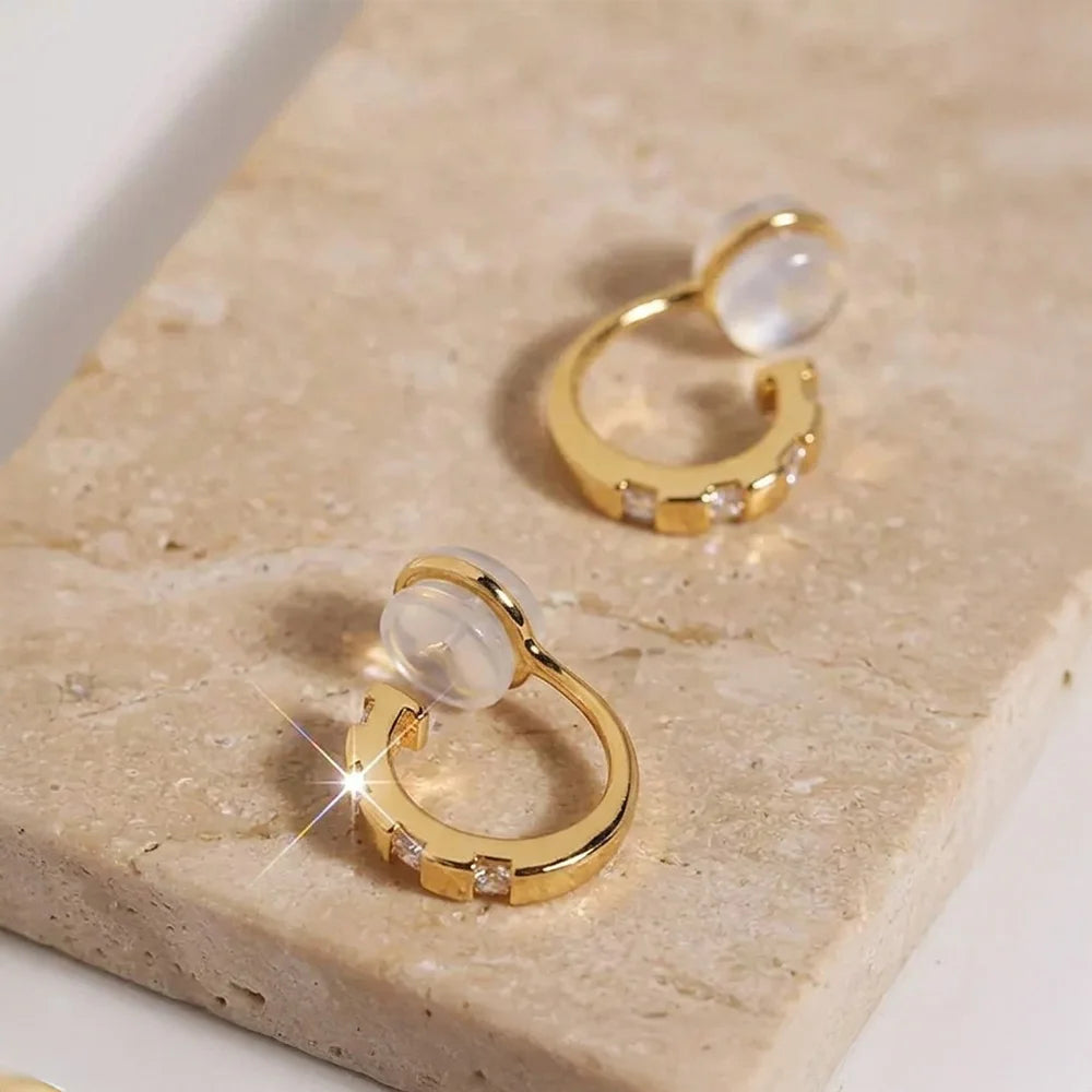 Close-up of yellow gold finished CZ clip-on huggies on a stone surface, highlighting the sparkle and comfort c-type clip on.