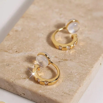 Close-up of yellow gold finished CZ clip-on huggies on a stone surface, highlighting the sparkle and comfort c-type clip on.