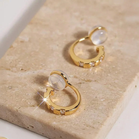 Close-up of yellow gold finished CZ clip-on huggies on a stone surface, highlighting the sparkle and comfort c-type clip on.