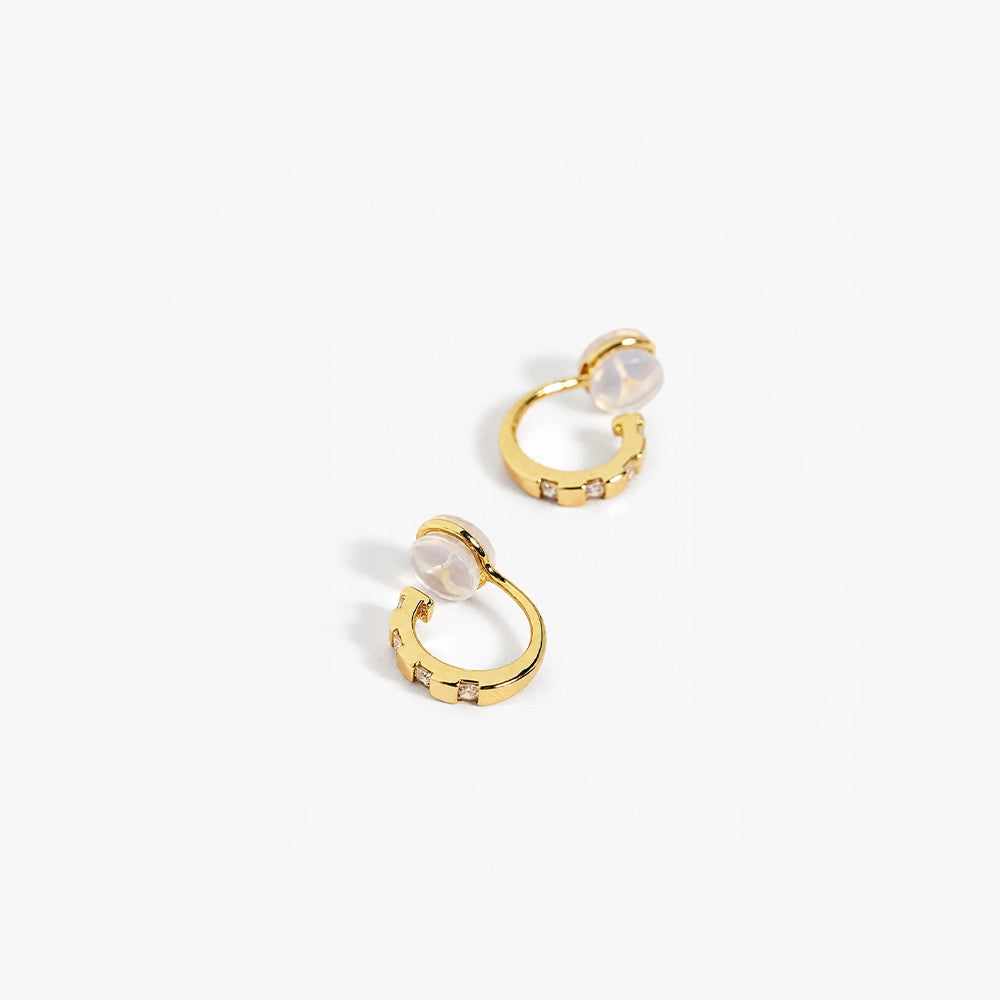Close-up of yellow gold finished CZ clip-on huggies on a stone surface, highlighting the sparkle and comfort c-type clip on.