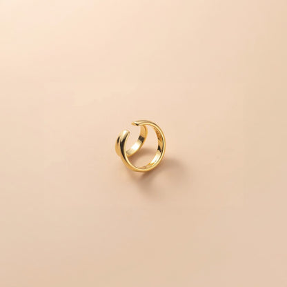 A solitary gold Dual Loop Ear Cuff sits on a peach-toned backdrop, offering a minimalistic yet striking look. This conch ear cuff is suitable for everyday wear, bringing a modern twist to even the simplest of outfits without the need for piercing.