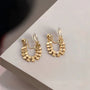 Pair of gold honeycomb clip-on hoop earrings angled to show the clear hexagonal patterns on a white surface.