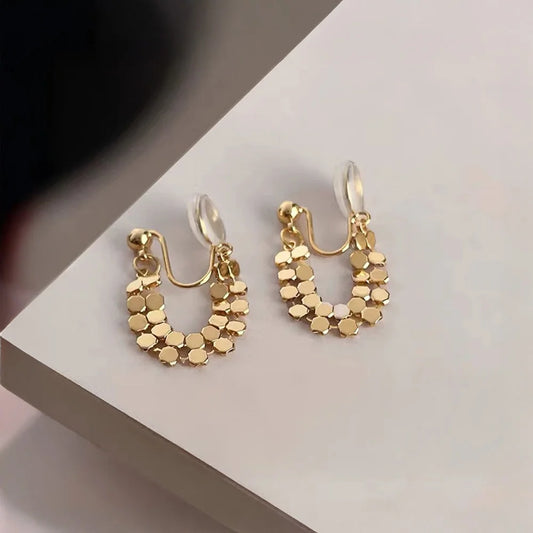 Pair of gold honeycomb clip-on hoop earrings angled to show the clear hexagonal patterns on a white surface.