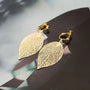 Gold leaf clip on earrings with filigree detail displayed on dark surface