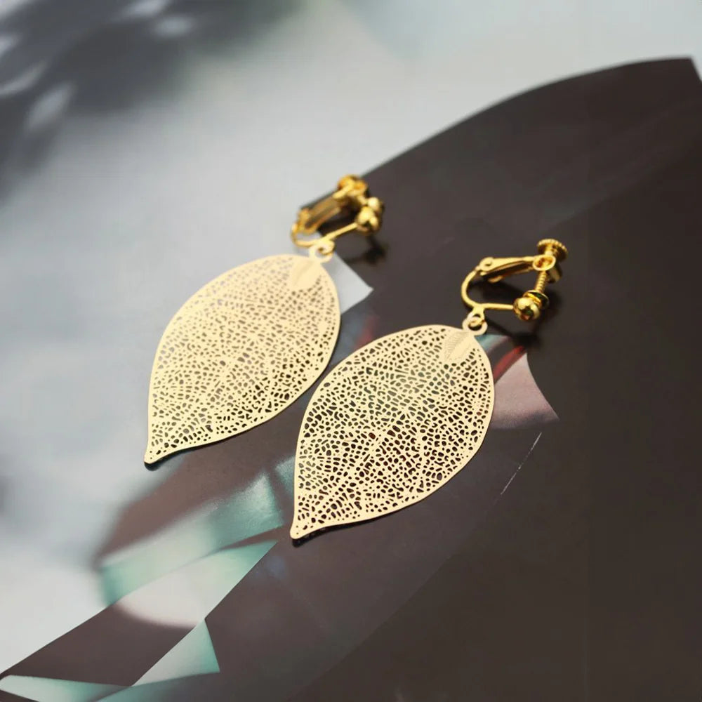 Gold leaf clip on earrings with filigree detail displayed on dark surface