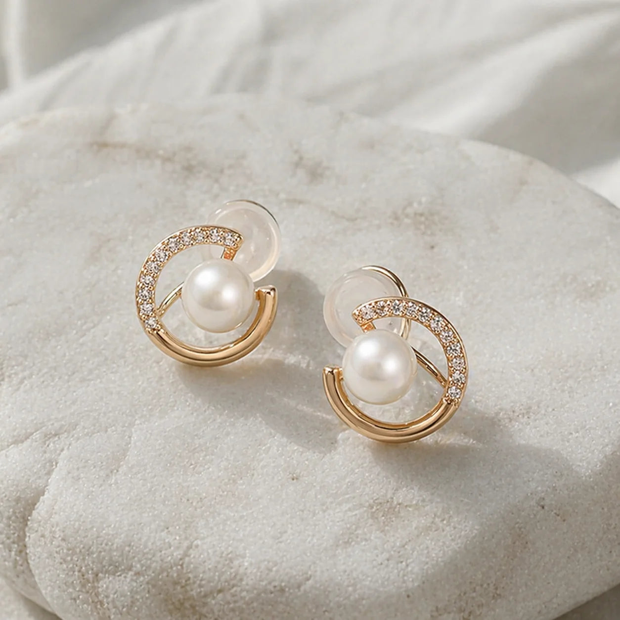 Pair of gold-plated pearl crescent clip on earrings featuring sparkling cubic zirconia on a white stone background.