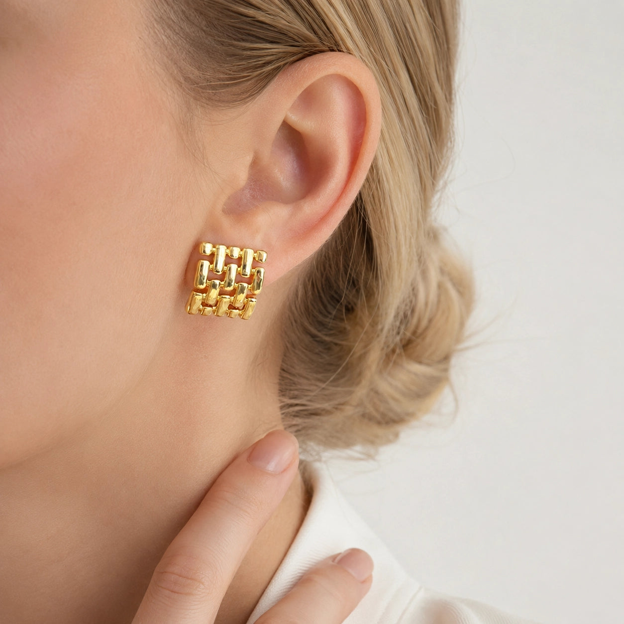 Woman wearing a gold woven square clip on earring on a non pierced ear