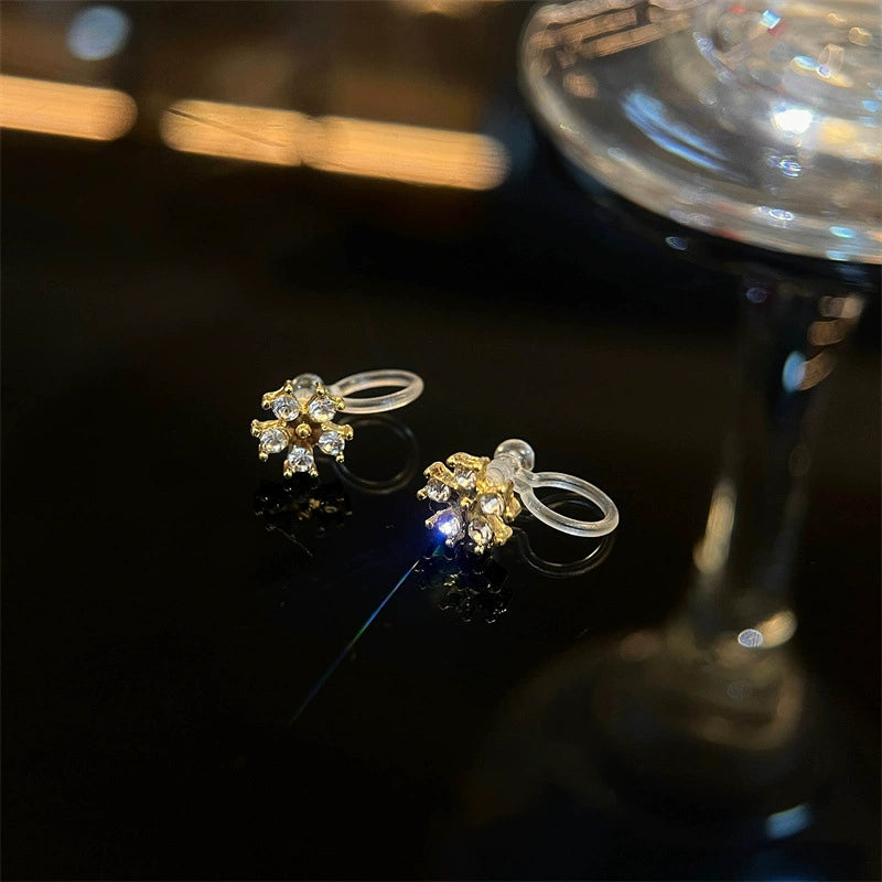 A close-up of the Golden Snowflake Crystal invisible clip-on earrings, highlighting the brilliant cubic zirconia and clear resin clip mechanism on a dark, reflective surface.