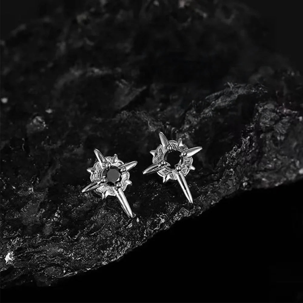 A pair of gothic star magnetic stud earrings with black centers, placed on a textured black rock surface, emphasizing their rugged aesthetic.