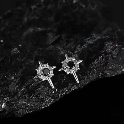 A pair of gothic star magnetic stud earrings with black centers, placed on a textured black rock surface, emphasizing their rugged aesthetic.