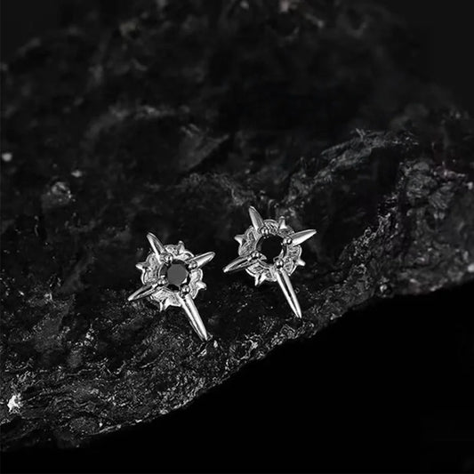 A pair of gothic star magnetic stud earrings with black centers, placed on a textured black rock surface, emphasizing their rugged aesthetic.