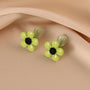 Lime Blossom Clip-On Earrings with yellow beaded flowers and black centers on neutral beige fabric background