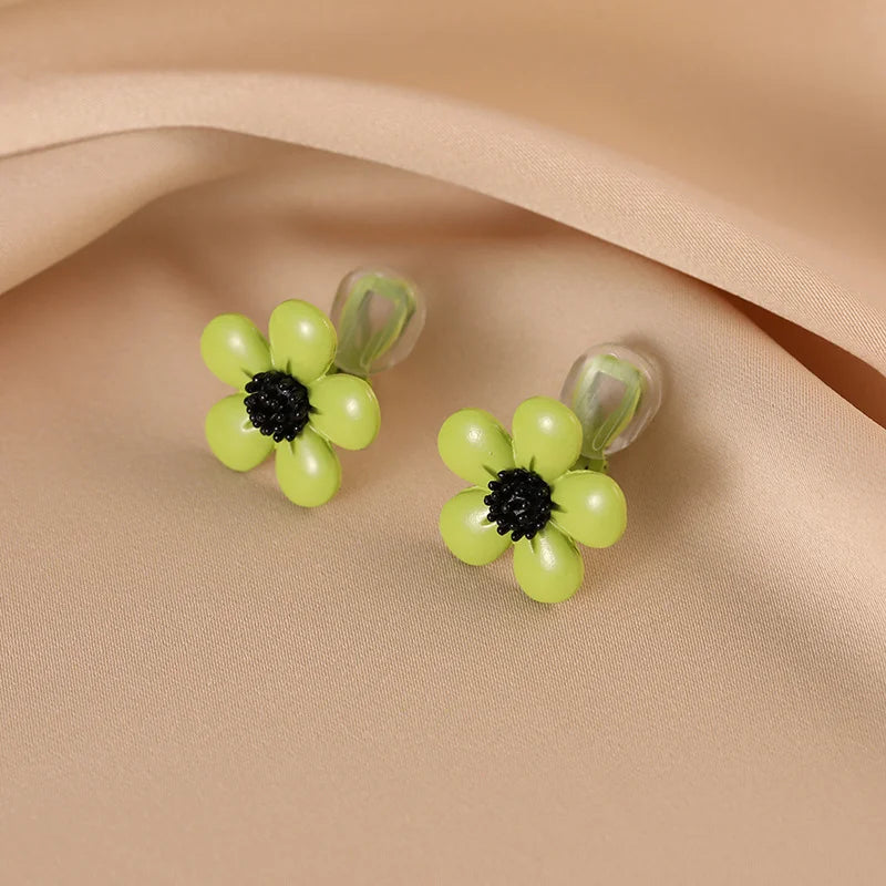 Lime Blossom Clip-On Earrings with yellow beaded flowers and black centers on neutral beige fabric background