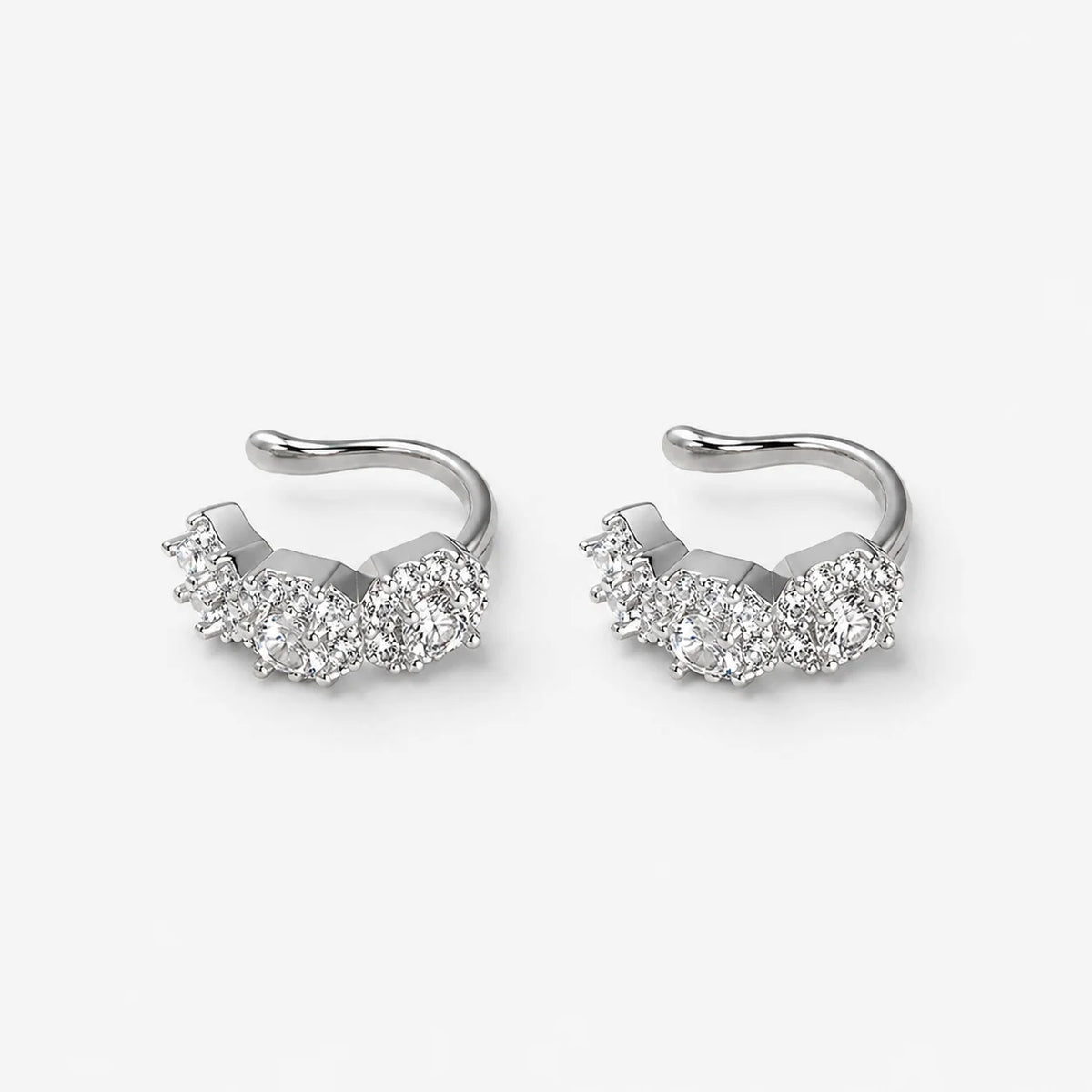 A pair of silver-toned huggie hoop earrings with a cluster of clear pavé-set round gemstones, shown on a light gray background.