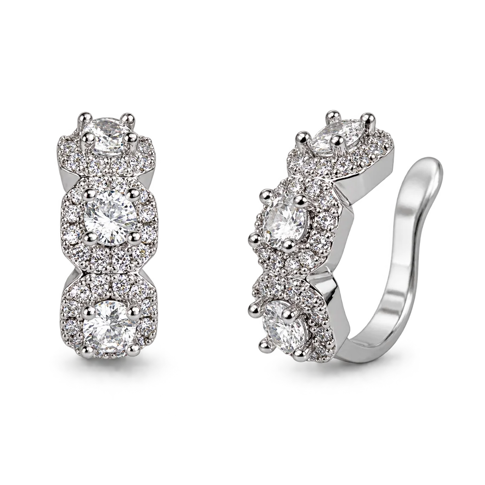 A pair of silver huggie hoop earrings with three stacked oval-cut clear gemstones, each surrounded by a halo of smaller clear stones, shown on a plain white background.