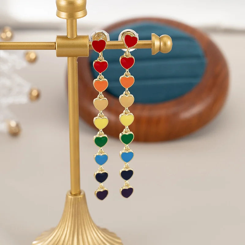 Rainbow Heart Cascade Clip On Earrings displayed on gold stand showing colorful enamel hearts in rainbow order from red to purple