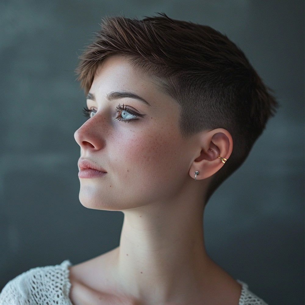 A side profile of a woman with short hair wearing a gold Helix Cross Ear Cuff on her right ear. The conch ear cuff's gleaming gold finish stands out against her skin, ideal for a romantic date or a special evening event, requiring no piercings for an effortless, chic look.