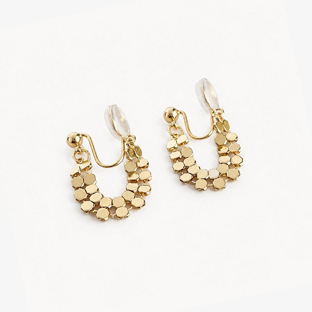 Pair of gold honeycomb clip-on hoop earrings angled to show the clear hexagonal patterns on a white surface.