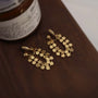 Geometric gold hexagonal clip-on earrings displayed on a rich, dark wood surface.