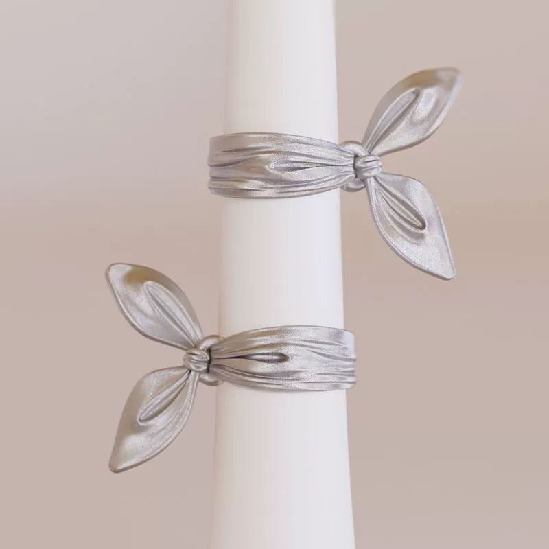 Gros plan sur le bracelet manchette en ruban argenté éclatant sur une surface neutre, mettant en valeur la finition miroir et les courbes fluides et effilées du nœud.