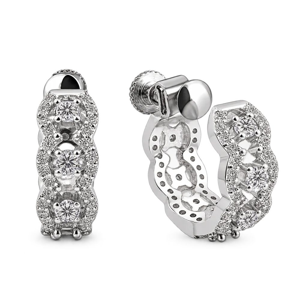 A pair of silver huggie hoop earrings adorned with multiple round-cut and pavé-set clear stones, shown from both the front and side angles on a white background.