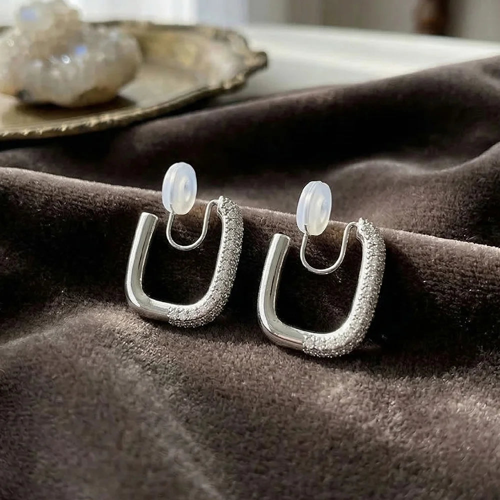 Two silver pave clip-on hoop earrings resting on a brown velvet surface, showcasing the shimmering stones and the soft silicone pads on the clips.