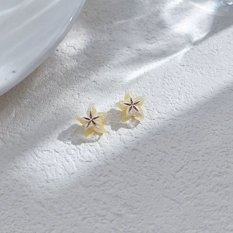 Two Tropical Star Fruit Magnetic Stud Earrings displayed on a textured white surface, with dappled sunlight, highlighting their vibrant yellow color.