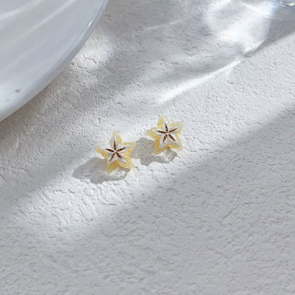 Two Tropical Star Fruit Magnetic Stud Earrings displayed on a textured white surface, with dappled sunlight, highlighting their vibrant yellow color.