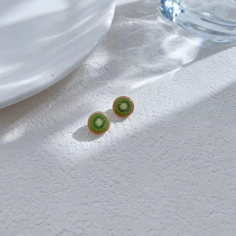 Two Sweet Kiwi Magnetic Stud Earrings displayed on a textured white surface, with dappled sunlight, highlighting their vibrant green color.
