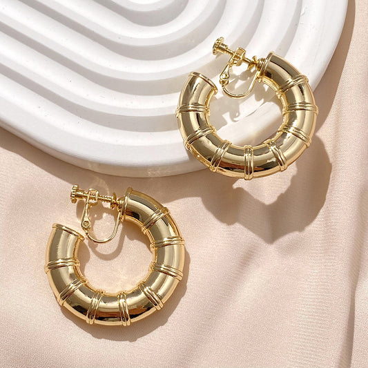 The Bamboo Hoop Clip-On Earrings feature a nature-inspired design in a gold-tone alloy with a comfortable screw-back closure, ideal for adding a touch of iconic style to any ensemble.