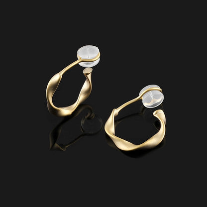 A diagonal view of matte gold sculptural clip on hoop earrings, showing the comfort pad and c-type clip on closure detail.