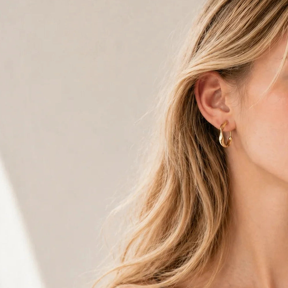 A office lady model wearing matte gold sculptural wavy clip on earrings, showing her professional look.