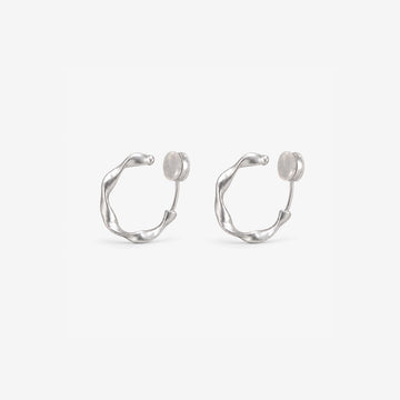 A pair of matte silver organic abstract clip-on hoop earrings with a soft satin finish.