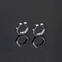A stylish product shot of the men's titanium steel clip-on huggie earrings in silver on a reflective black surface.
