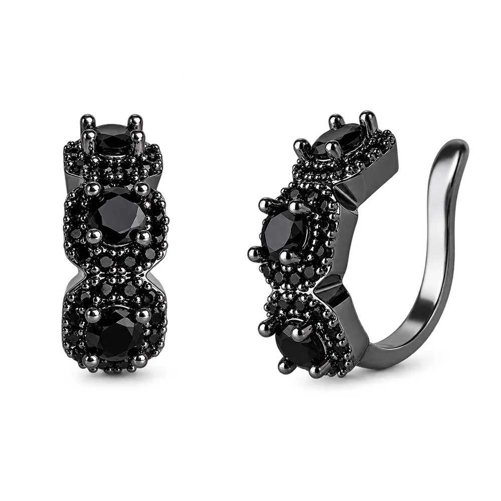 A pair of black huggie hoop earrings with three round black gemstones in prong settings, surrounded by small black pavé accents, shown on a plain white background.
