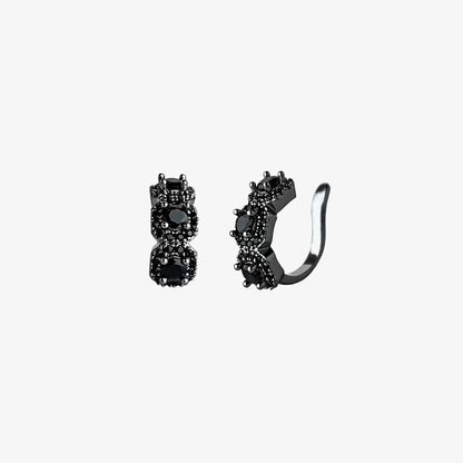 A studio shot of a pair of Midnight Star black triple zircon pavé clip-on ear cuffs on a clean white background, highlighting their dark sparkle and intricate details.
