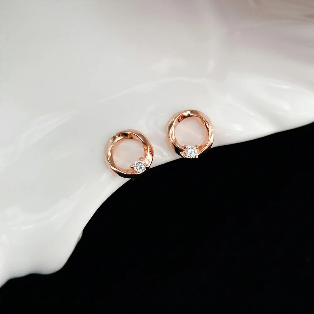 Dainty minimalist open halo earrings in rose gold with a shimmering crystal focal point displayed on a white surface.