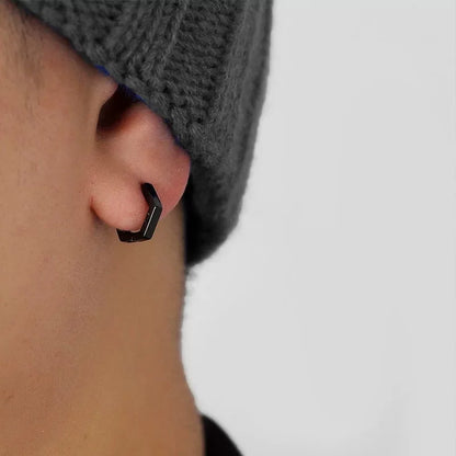 A close-up of a model wearing a single black hexagon clip-on earring on his earlobe for a minimalist, non-pierced look.