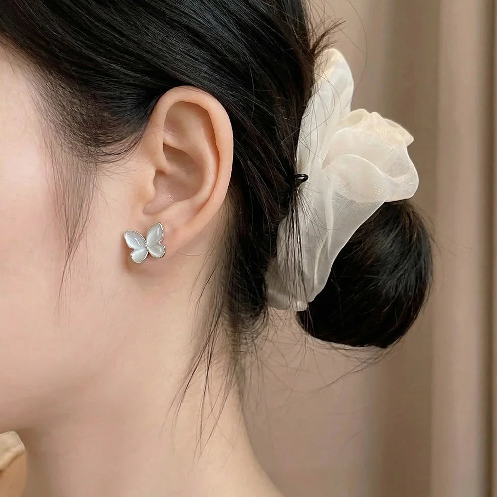 A close-up of a woman wearing an iridescent silver butterfly stud earring, showcasing the ethereal glow against a soft background.