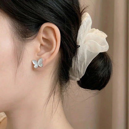 A close-up of a woman wearing an iridescent silver butterfly stud earring, showcasing the ethereal glow against a soft background.