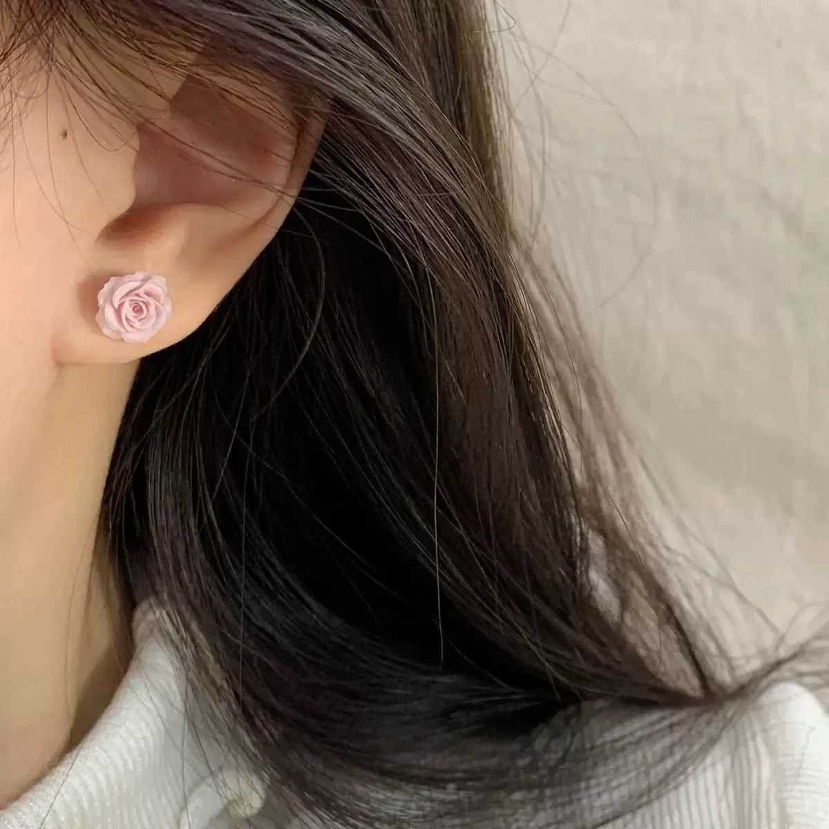 A close-up of a model's ear wearing a single pink rose magnetic stud earring, demonstrating its subtle size and placement on the earlobe.