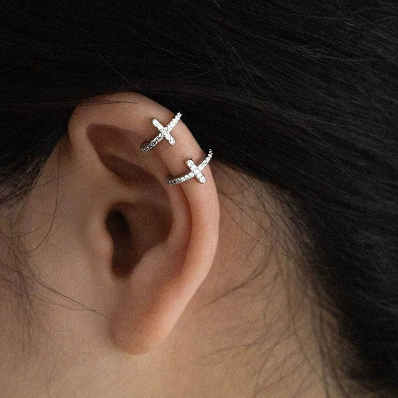 A model's ear featuring two silver pavé cross clip-on ear cuffs, demonstrating how they look as part of an edgy ear stack.