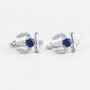 A pair of silver-toned huggie earrings featuring a central round-cut deep blue gemstone and small clear pavé accents, photographed on a clean white background.