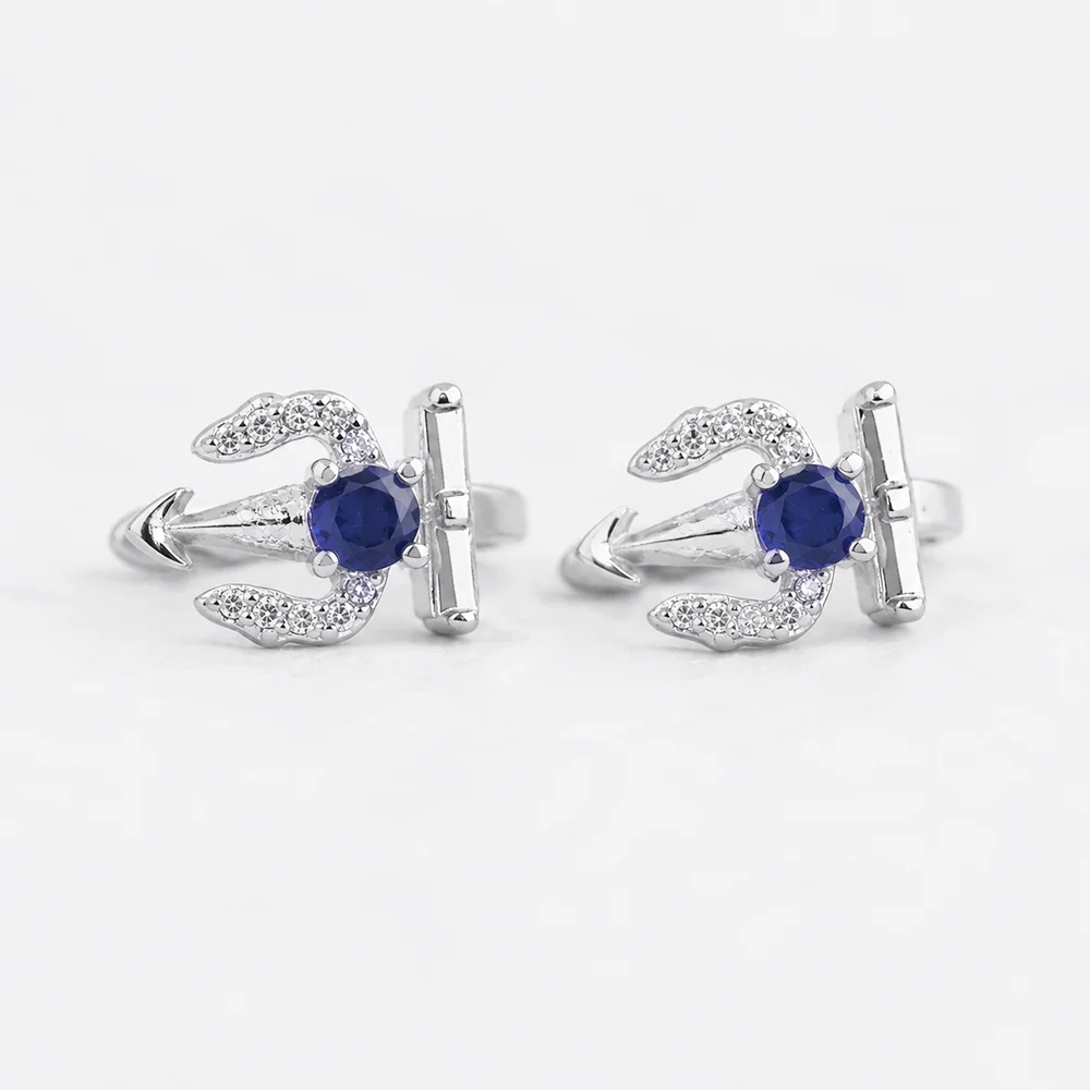 A pair of silver-toned huggie earrings featuring a central round-cut deep blue gemstone and small clear pavé accents, photographed on a clean white background.