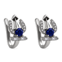 A pair of silver-toned huggie hoop earrings featuring a central round-cut blue sapphire, surrounded by small clear cubic zirconia stones in a crescent shape, with a small rectangular bar of baguette-cut clear stones at the bottom, shown on a plain white background.