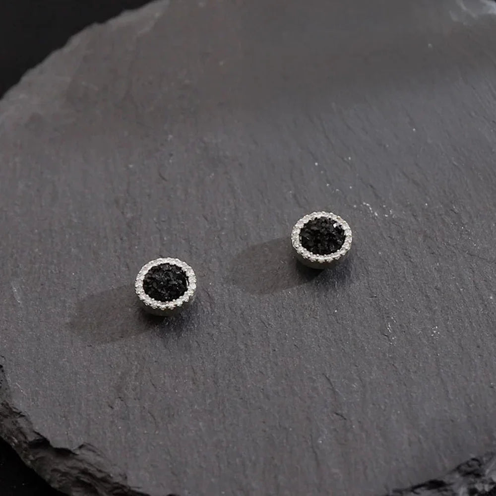 A pair of Nightfall Pavé black crystal magnetic stud earrings, showcasing their sparkling design on a dark slate surface.