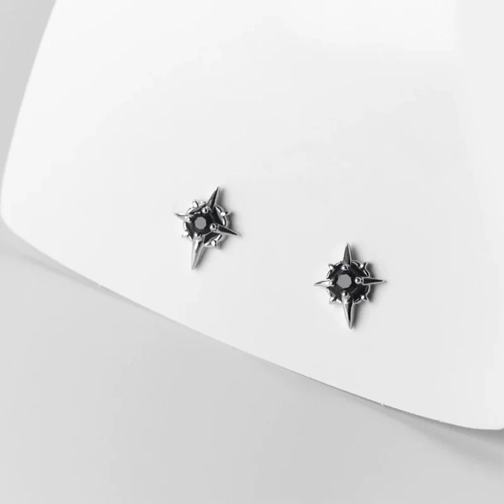 A pair of no-piercing compass rose style magnetic earrings with black stones, resting on a white surface to highlight their clean design.