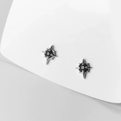 A pair of no-piercing compass rose style magnetic earrings with black stones, resting on a white surface to highlight their clean design.
