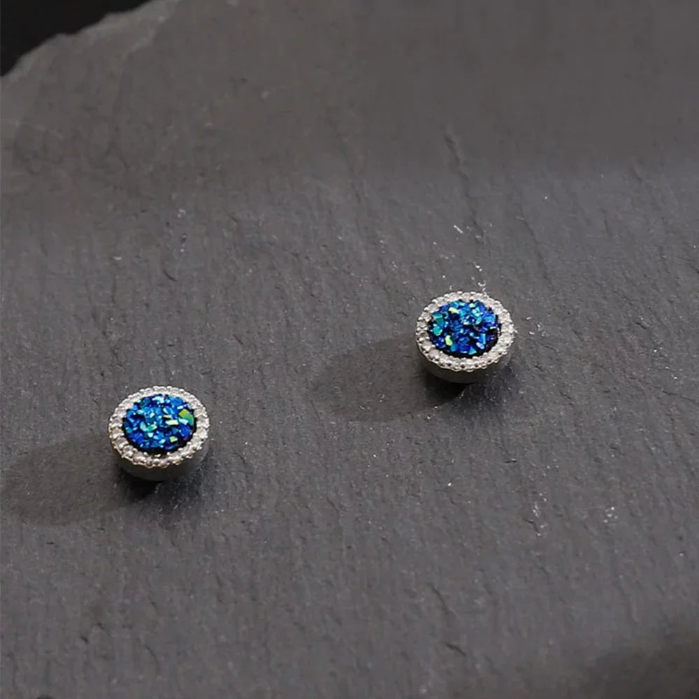 A pair of Nova Iridescent Blue Galaxy Magnetic Stud Earrings, showcasing their sparkling blue druzy texture on a dark slate background.